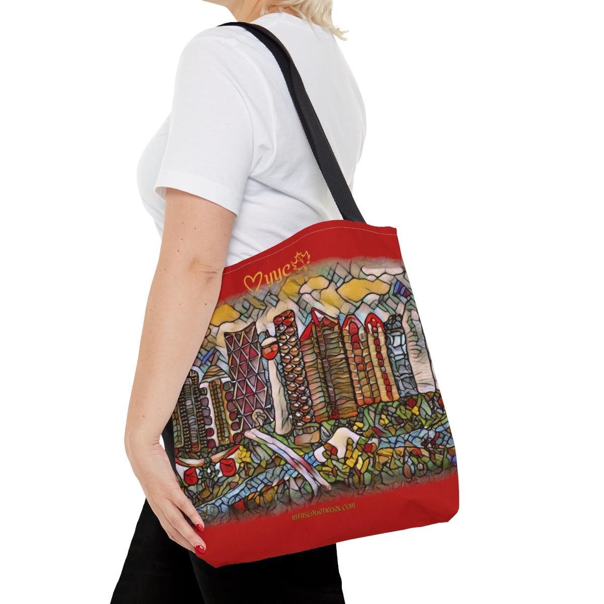 red tote bag on womans shoulder. has artwork of city of calgary