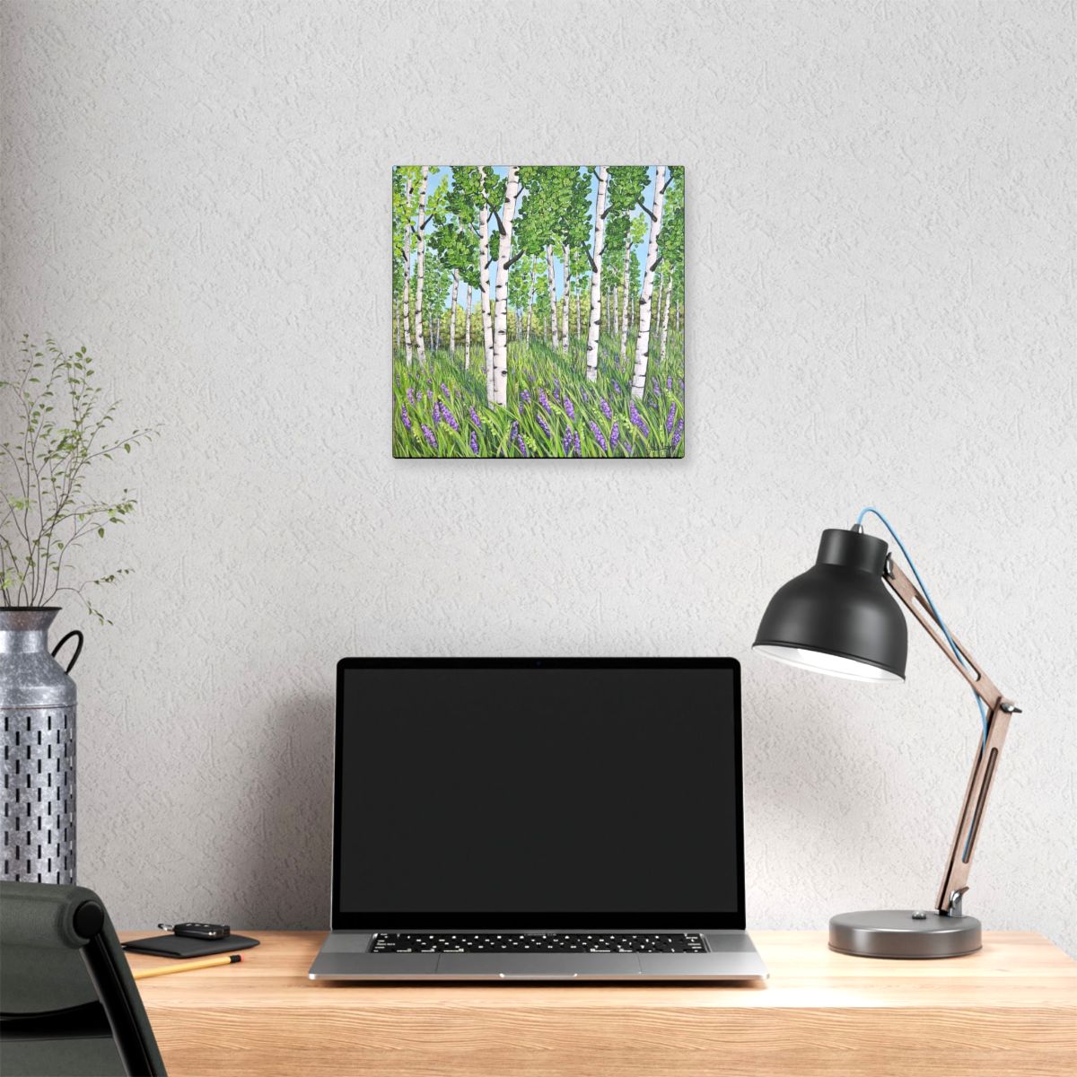 Laptop on a desk with a painting of a forest scene above it.